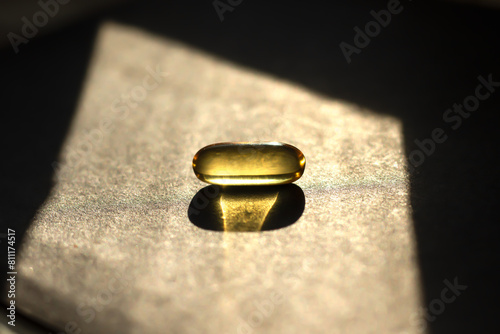A yellow pill on a black background in bright sunlight. Close-up with a blurred background.