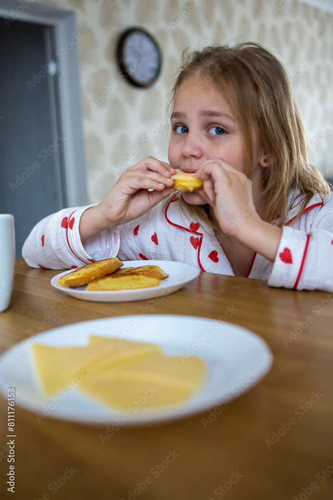 A pretty blonde girl in beautiful pajamas is sitting at a cozy table in the kitchen and eating a delicious and healthy breakfast. The concept of proper and balanced nutrition. A pretty blonde girl in beautiful pajamas is sitting at a cozy table in the kitchen and eating a delicious and healthy breakfast. The concept of proper and balanced nutrition.