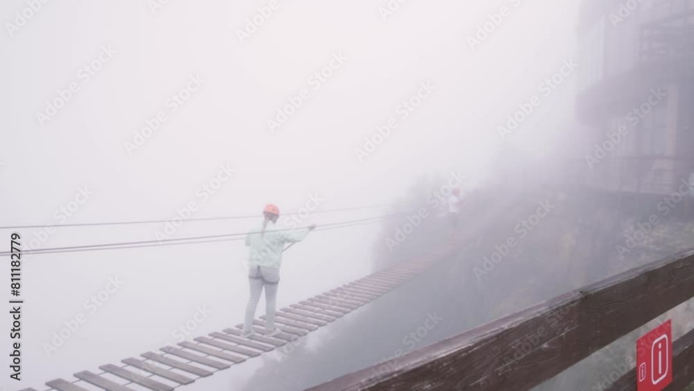 two unrecognizable people walking on suspension hanging rope bridge in deep fog two unrecognizable people walking on suspension hanging rope bridge in deep fog