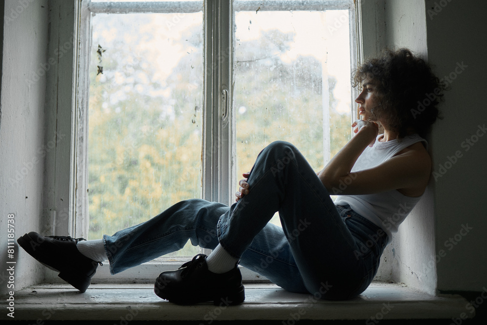 photograph of a curly-haired girl who sits near the window and looks straight ahead. Grain effect used