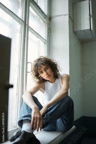 Free Download photograph of a curly-haired girl who sits near the window and looks straight into the camera. Grain effect used - GFXLoad