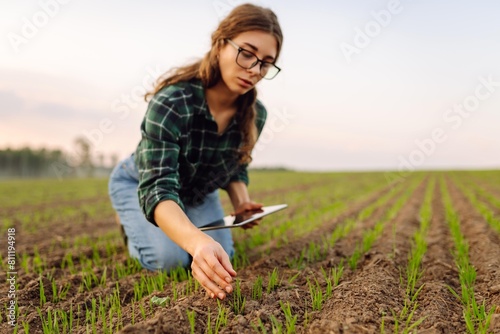 Smart farmer woman agronomist checks young sprout the field with tablet. Intelligent agriculture and digital agriculture.