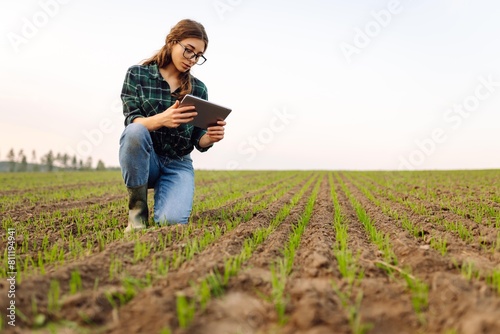 Smart farmer woman agronomist checks young sprout the field with tablet. Intelligent agriculture and digital agriculture. © maxbelchenko