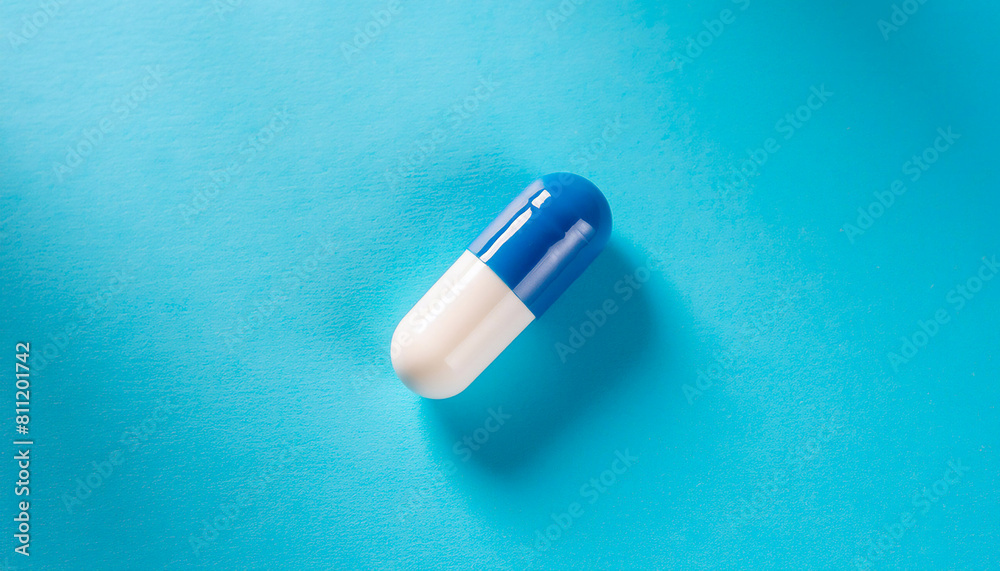 Close-up single white and blue capsule isolated on light blue background, diagonal direction, top view, in center, copy space Close-up single white and blue capsule isolated on light blue background, diagonal direction, top view, in center, copy space