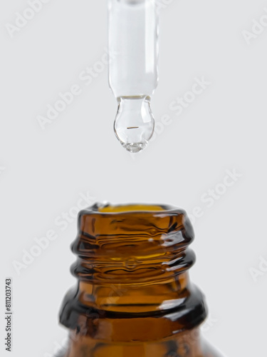 Glass pipette filled with cosmetic serum and a yellow glass bottle close-up on a grey background