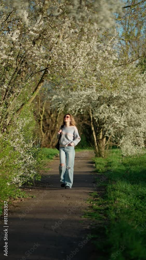 Woman enjoys spring walk among flowers. Woman walks along path in park surrounded by flowering trees. Concept of Spring, nature, pleasure. Woman enjoys spring walk among flowers. Woman walks along path in park surrounded by flowering trees. Concept of Spring, nature, pleasure.