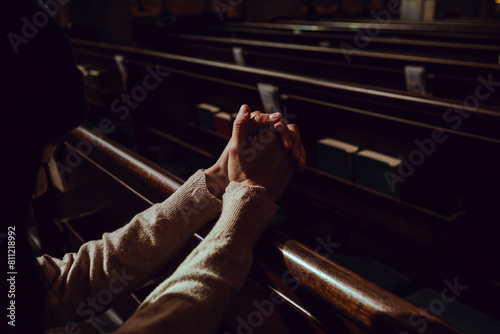 Quadro su tela Close-up view of a woman's clasped hands as she prays in a church pew, emphasizing a personal and intimate spiritual moment