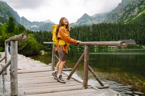 Woman traveler with yellow hiking backpack and hiking stiks enjoys the scenery. Active lifestyle. Wanderlust. photo