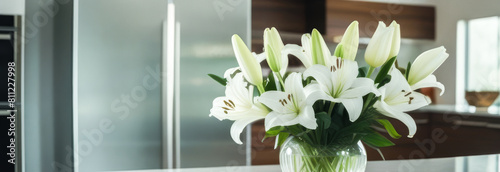 A banner bouquet of white lilies in a transparent vase on the table in a white modern kitchen. creating a cozy home. free space for text