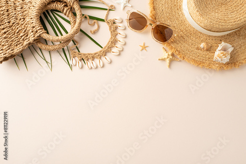 Fototapeta Naklejka Na Ścianę i Meble -  Seaside serenity scene: Top view shot showcasing sunhat, sunglasses, beach bag, island accessories, palm branch, seashells, starfish on pastel beige base, with available area for text or advertising