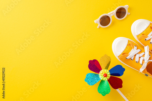 A vibrant summer themed photo featuring a colorful pinwheel, orange sneakers, and white sunglasses laid out on a yellow background