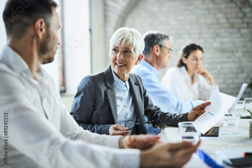 Happy senior businesswoman talking about reports with her colleague on a meeting in the office.