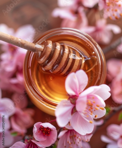 jar of honey with honey stick and bright flowers on a light background