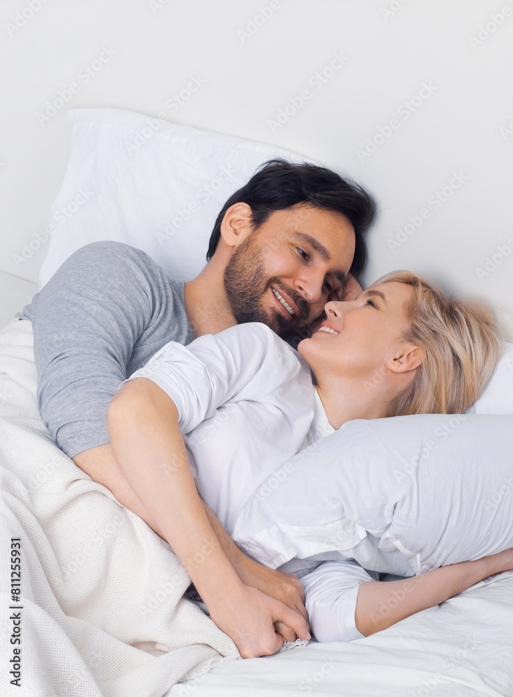 Image of young playful couple pair looking at each other, lay on home bed. Blond woman, brunette man in love, happy family, flirting, planning pregnancy concept. Image of young playful couple pair looking at each other, lay on home bed. Blond woman, brunette man in love, happy family, flirting, planning pregnancy concept.