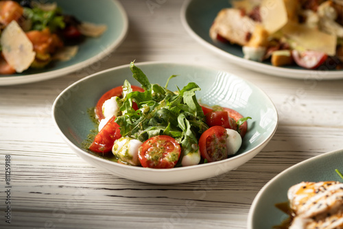 Italian caprese salad with tomatoes, mozzarella cheese, basil and olive oil serving on plate on table