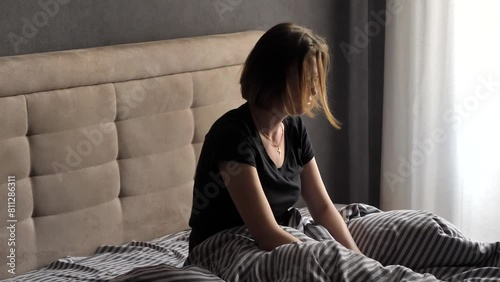 An upset woman freaks out and throws pillows while sitting on the bed. Emotional breakdown, bad morning. The girl woke up in no mood. Menstruation, Women's critical days.  photo
