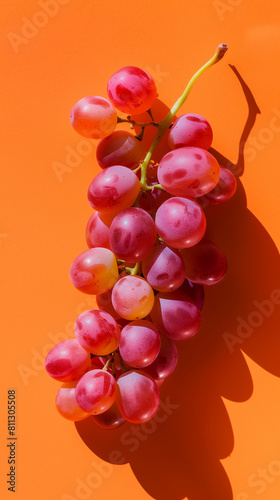 A cluster of luscious pink grapes arranged gracefully on an orange background, captured in a modern photography style. The soft pink hues of the grapes contrast beautifully with the warm tones 