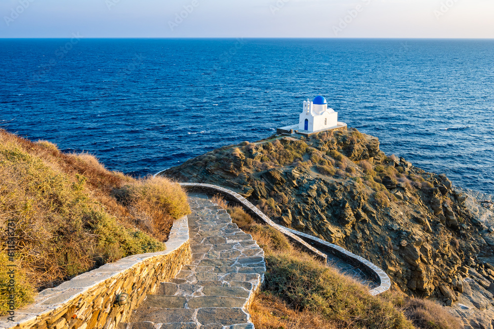 Coastal path with steps to small church built on rocks and blue sea in background in Kastro village, Sifnos island, Greece