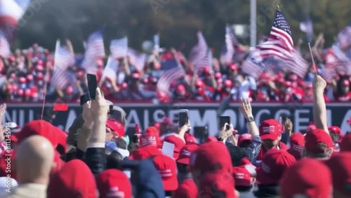 Crowds gather in a sea of red hats while waving American flags white watching a right wing candidate speak at a republican campaign rally. photo