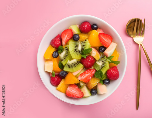 healthy fruit salad in a white bowl on pink background, colorful fruit