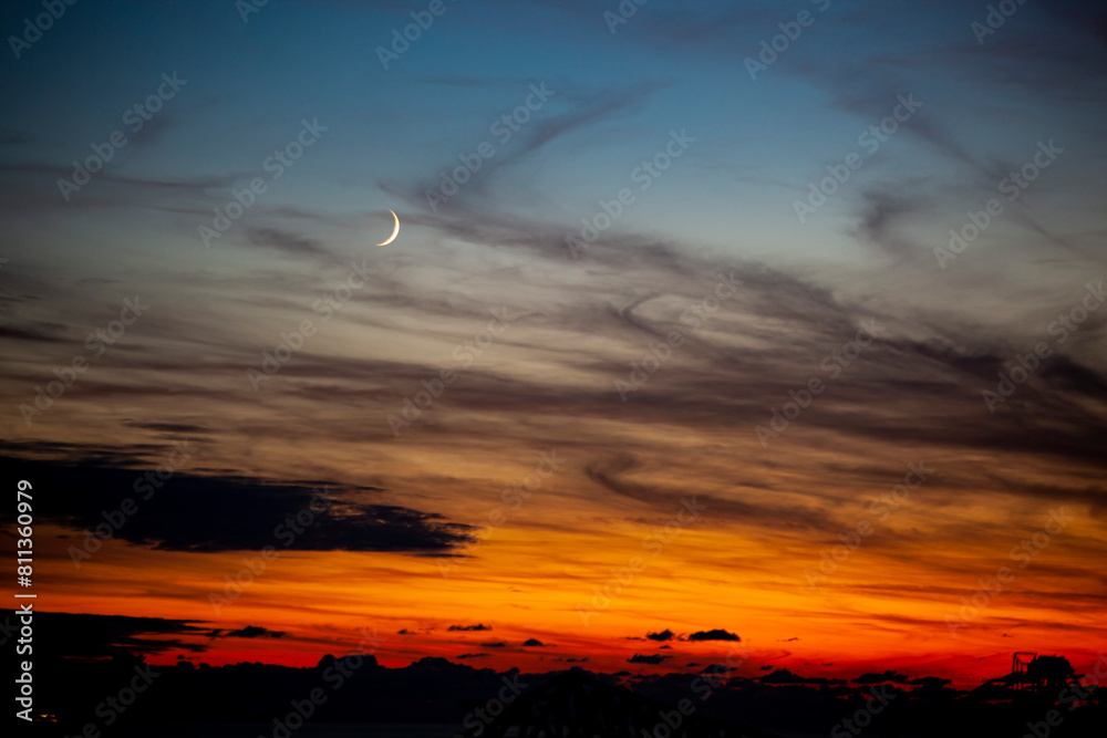 Red-orange sky at sunset in twilight evening with dark clouds and moon. Nature sky. Background, horizon golden sky, sunrise cloud magnificent, twilight sky.
