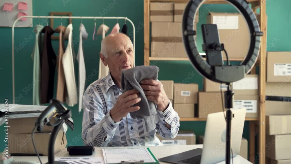Blogger SME business old man using mobile phone and video call for sell clothes, packing product at home office, entrepreneur in e-commerce