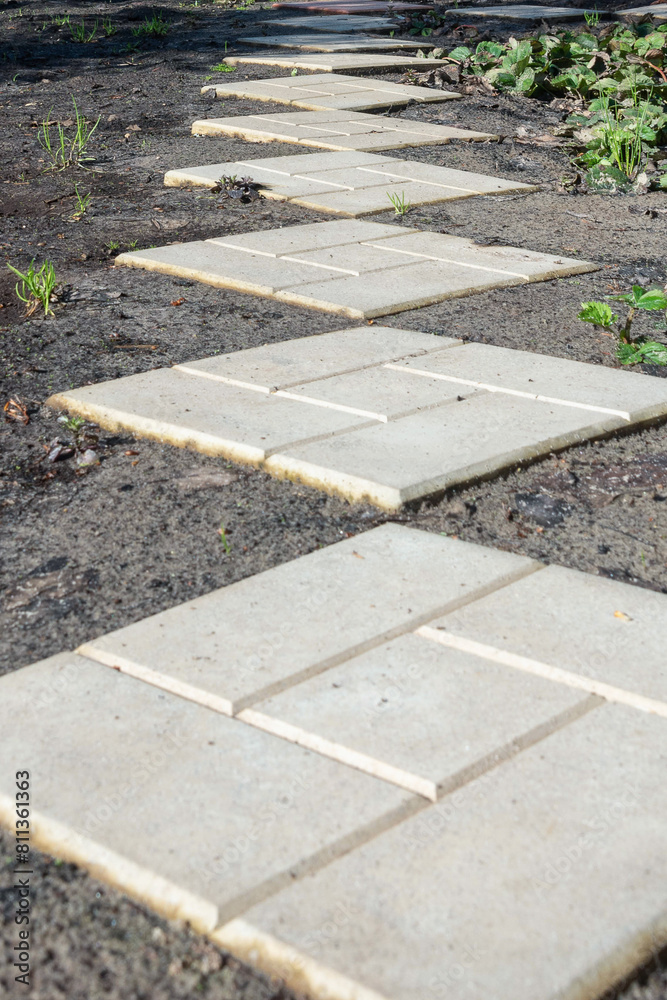 Obraz premium Perspective of concrete paving slabs on cottage garden ground.