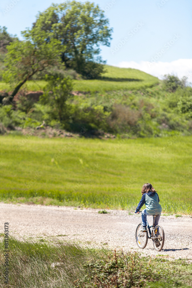 A young boy rides a bicycle down a dirt road in a grassy field A young boy rides a bicycle down a dirt road in a grassy field