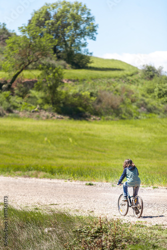 A young boy rides a bicycle down a dirt road in a grassy field