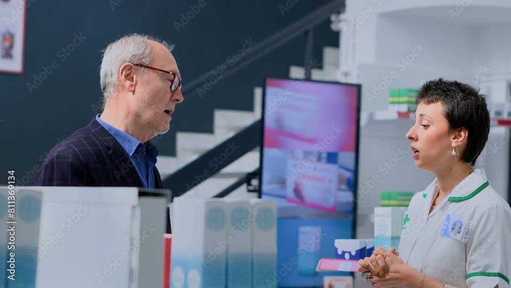Aged client in need of prescription illness prevention drug informations in apothecary, asking experienced pharmacist. Pharmacy worker helping elderly customer with pharmaceutical expertise Aged client in need of prescription illness prevention drug informations in apothecary, asking experienced pharmacist. Pharmacy worker helping elderly customer with pharmaceutical expertise