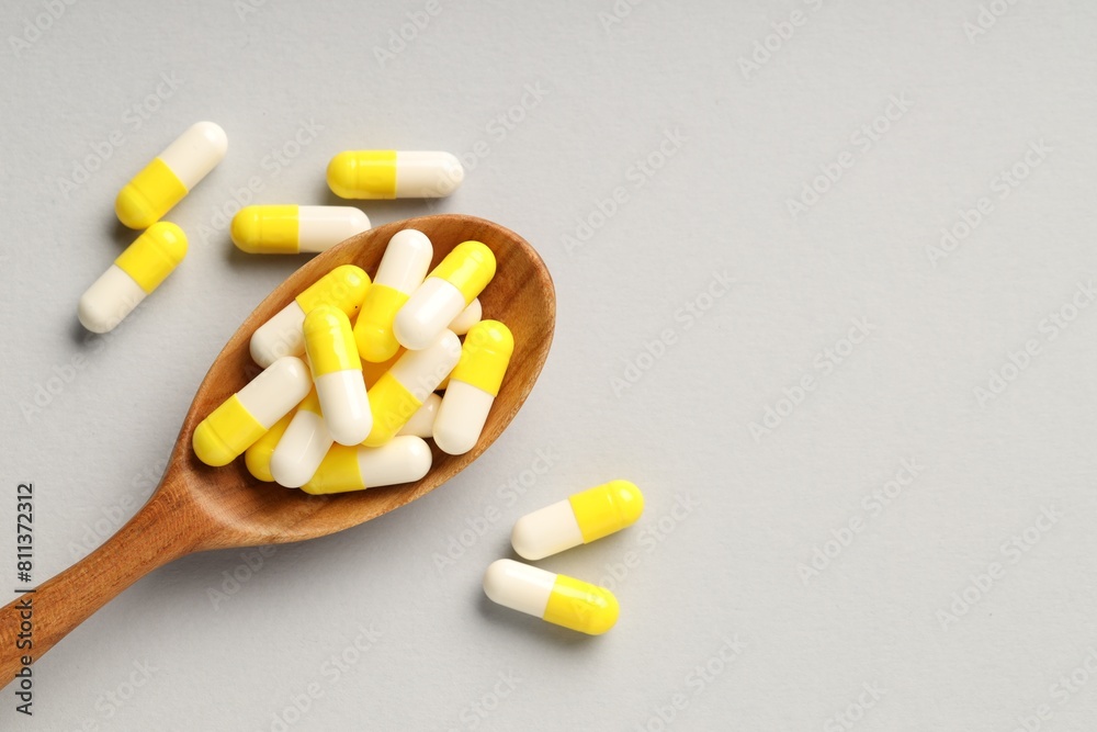 Many antibiotic pills with wooden spoon and space for text on grey background, top view. Medicinal treatment Many antibiotic pills with wooden spoon and space for text on grey background, top view. Medicinal treatment