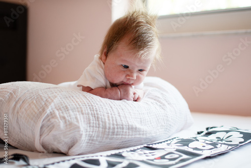 Little cute Caucasian baby girl doing tummy time. Tummy time for newborns on nursing pillow. High contrast learning cards for babies