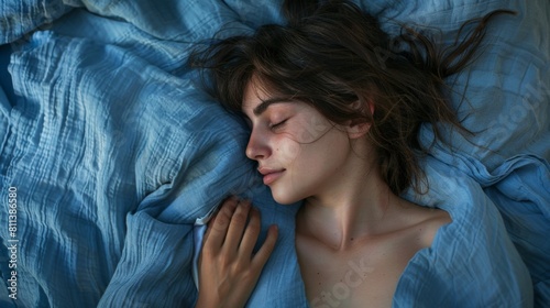 Woman sleeps with azure blanket draped over her, eyes shut peacefully. A woman with black hair is asleep under an azure blanket, her eyes closed and eyelashes resting on her cheeks.  photo