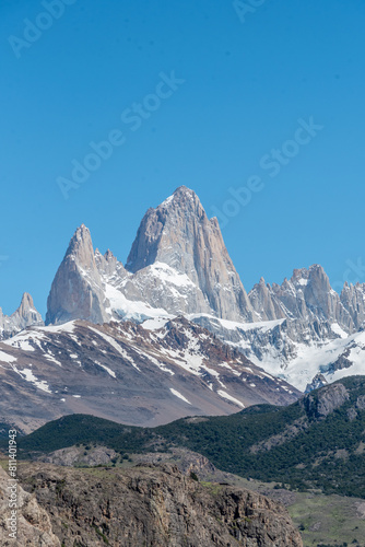 The Fitz Roy mountain range is covered in snow and the sky is clear and blue