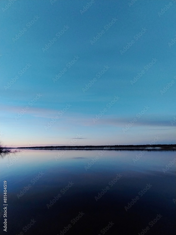 Realistic photograph of a calm lake at dusk, with a blue sky and calm water reflecting the clear sky.