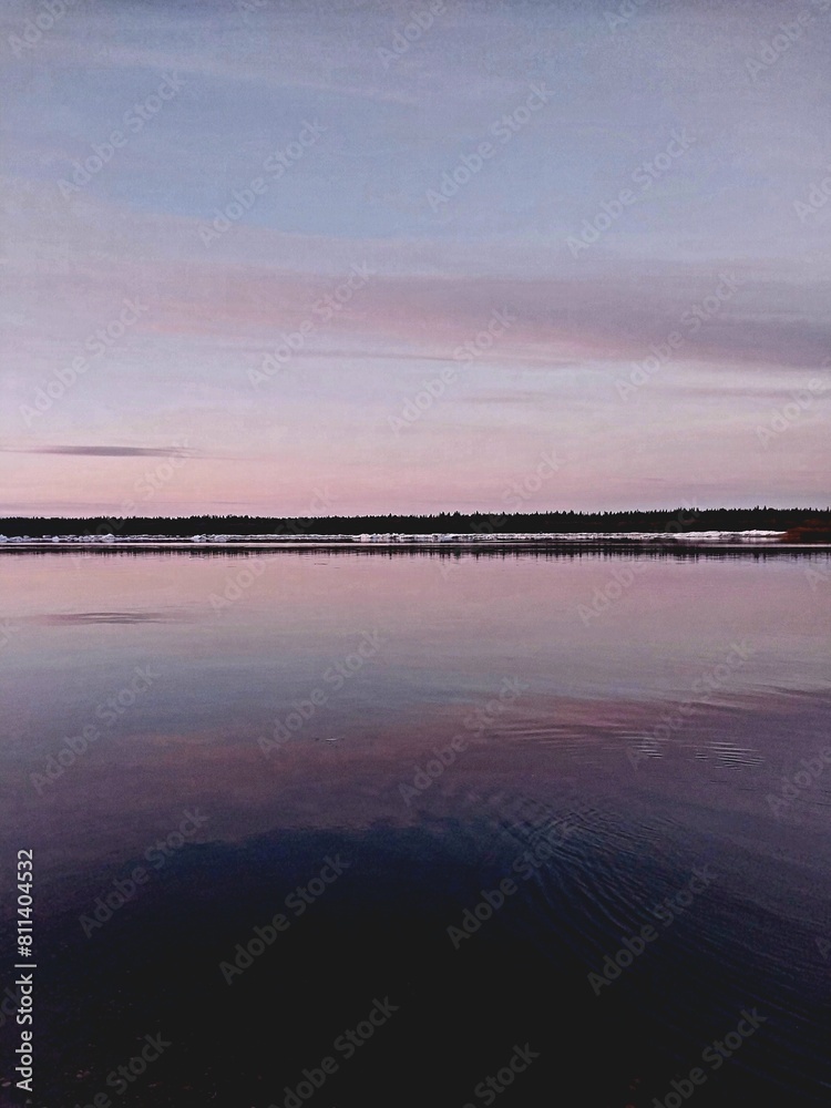 Obraz premium Realistic photo of the calm water surface at dusk, with distant reflections and a sky in shades of pink and purple. 