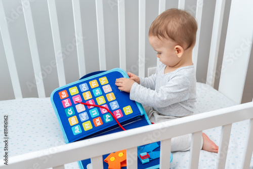 Little baby girl playing with busy book while sitting in crib. Concept of quiet books and modern educational toys