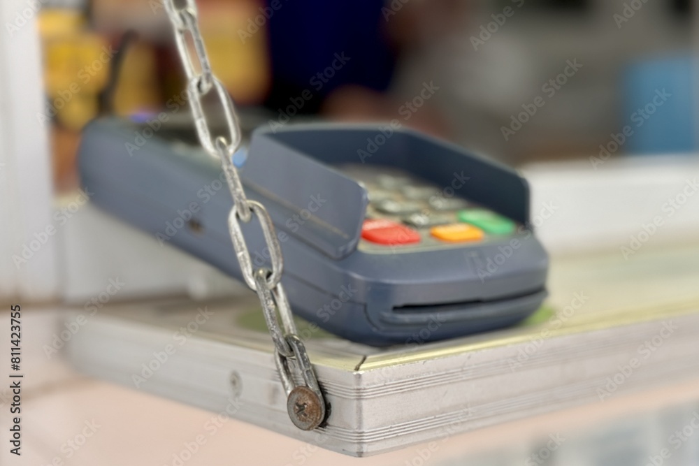 Close-up of a payment terminal for paying for goods with plastic cards lying on a shelf with an iron chain for cleaning it when closing a mobile grocery stall Close-up of a payment terminal for paying for goods with plastic cards lying on a shelf with an iron chain for cleaning it when closing a mobile grocery stall