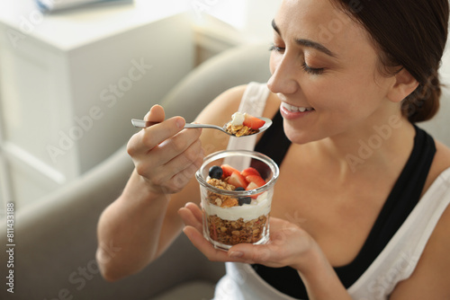 Woman eating tasty granola with fresh berries and yogurt at home