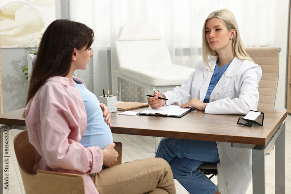 Doctor consulting pregnant patient at table in clinic Doctor consulting pregnant patient at table in clinic