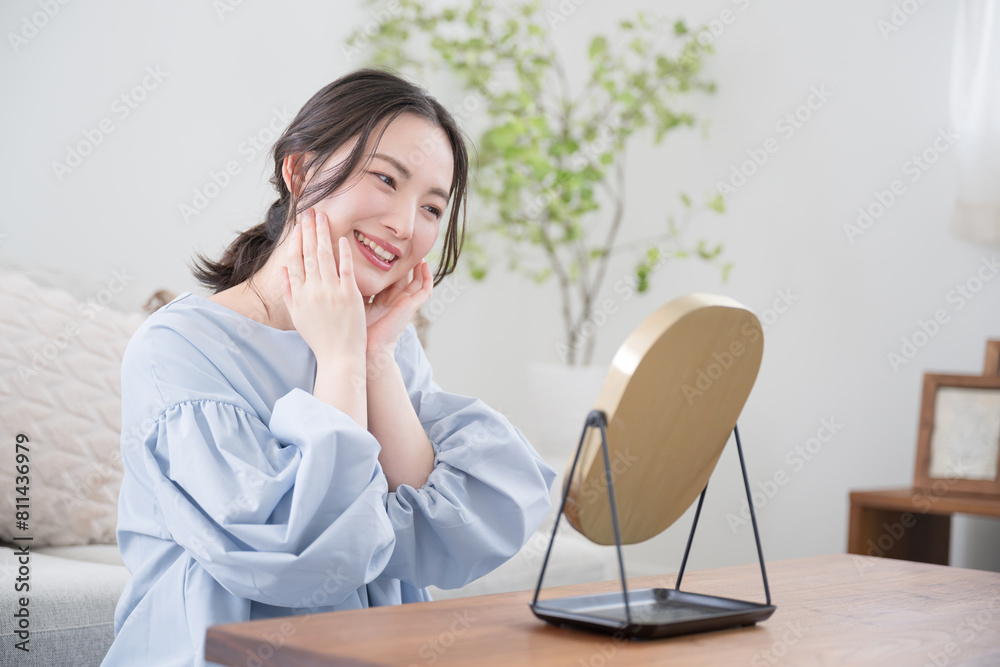 Close-up of the profile of a young woman with a pretty smile who looks in the mirror at her skin care in her room or living room and cares about her skin.
