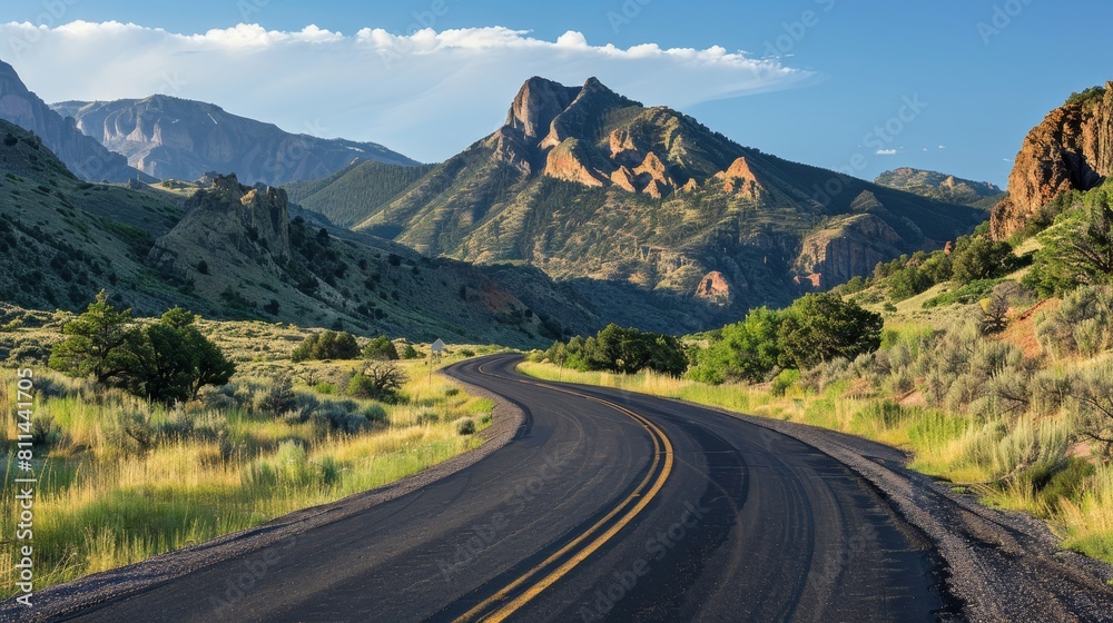 Fototapeta premium Country road winding through the landscape, rocky mountains towering in the background, under bright, clear lighting