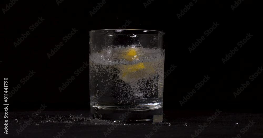 Slow motion shot of soda and lemons pouring into glass on black background. Slow motion shot of soda and lemons pouring into glass on black background.