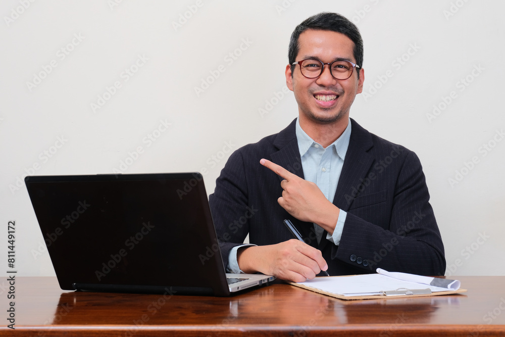A recruiter staff on his workplace smiling at the camera and pointing beside him A recruiter staff on his workplace smiling at the camera and pointing beside him