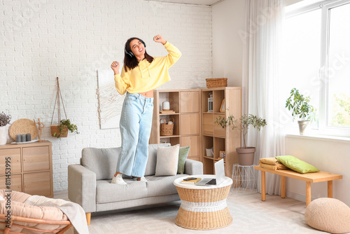 Beautiful young woman in stylish hoodie listening music and dancing at home