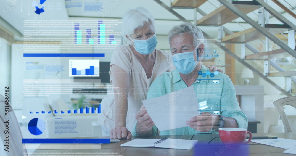 Fototapeta premium Image of statistical data processing over senior couple wearing face masks reading a document