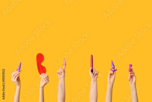 Female hands with different sex toys against yellow background