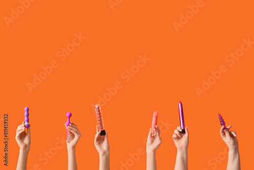 Female hands with different sex toys on orange background