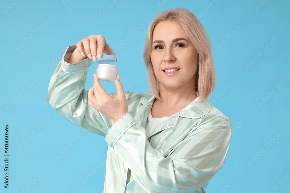 Beautiful mature happy woman with jar of face cream on blue background Beautiful mature happy woman with jar of face cream on blue background