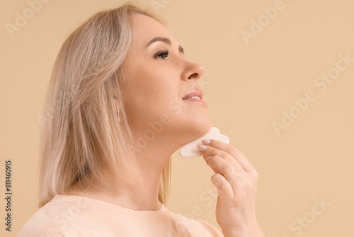 Beautiful mature woman with guasha tool on beige background